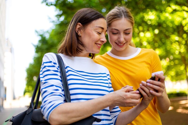 A mother and daughter looking at a phone together outdoors, warm light